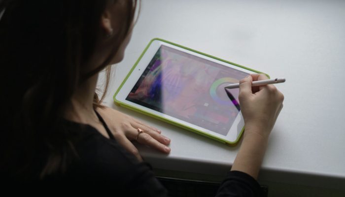 A woman uses a stylus pen on a tablet computer, creating digital art.